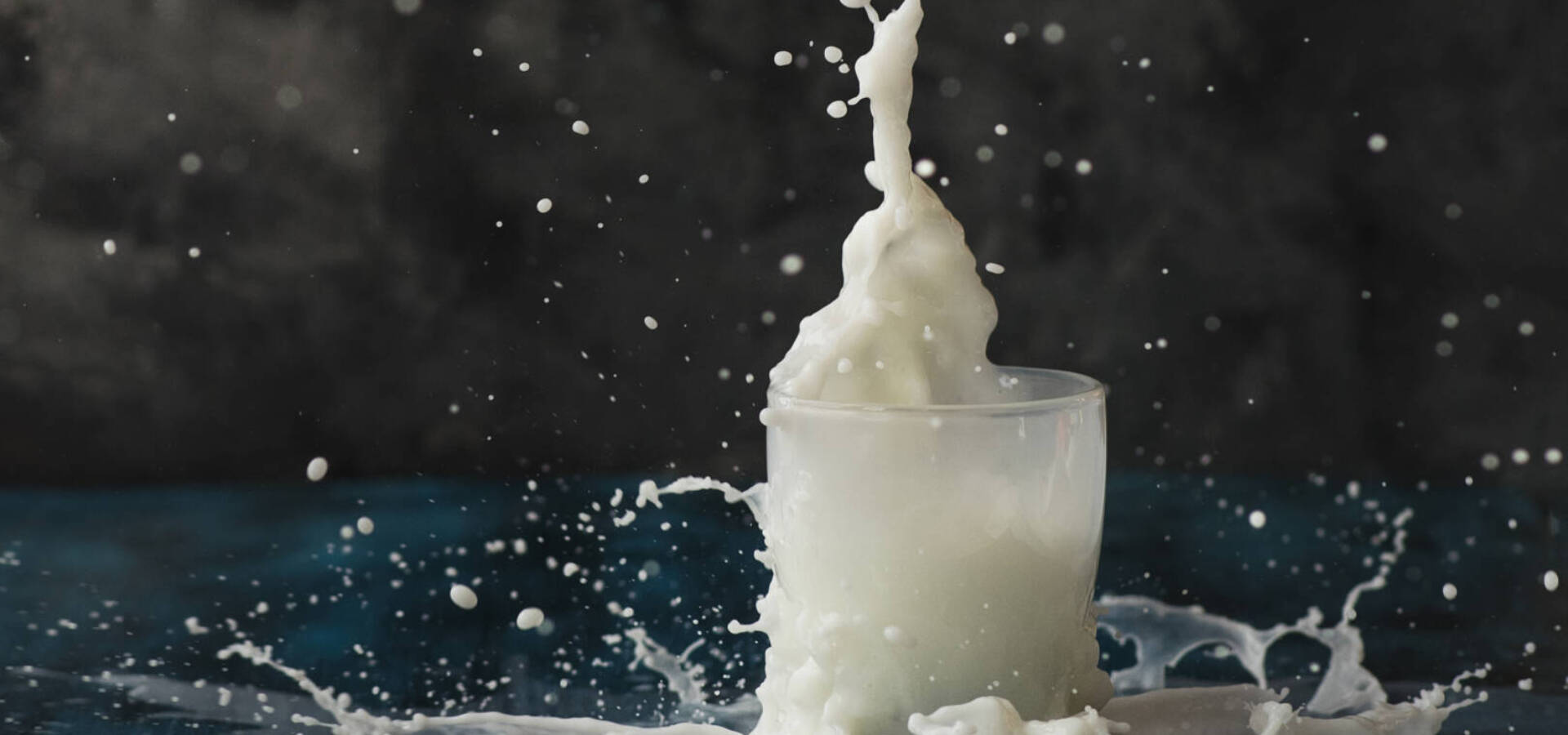 Splash of milk in a glass on dark background, fresh white drink